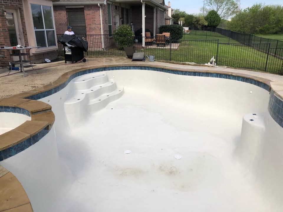 Empty swimming pool with white interior in a backyard beside a house