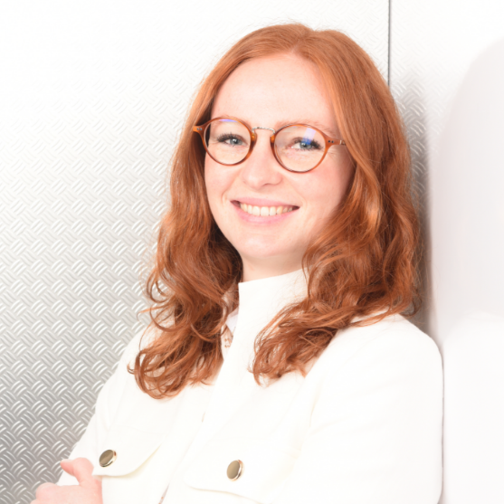 Eine Frau mit roten Haaren, trägt eine Brille und ein weißes Hemd