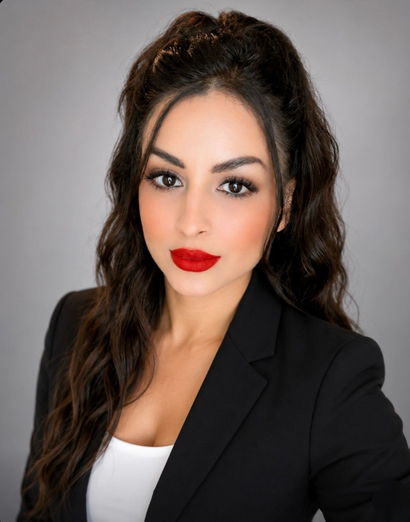 Woman in black blazer and white top with dark hair and red lipstick against a gray background