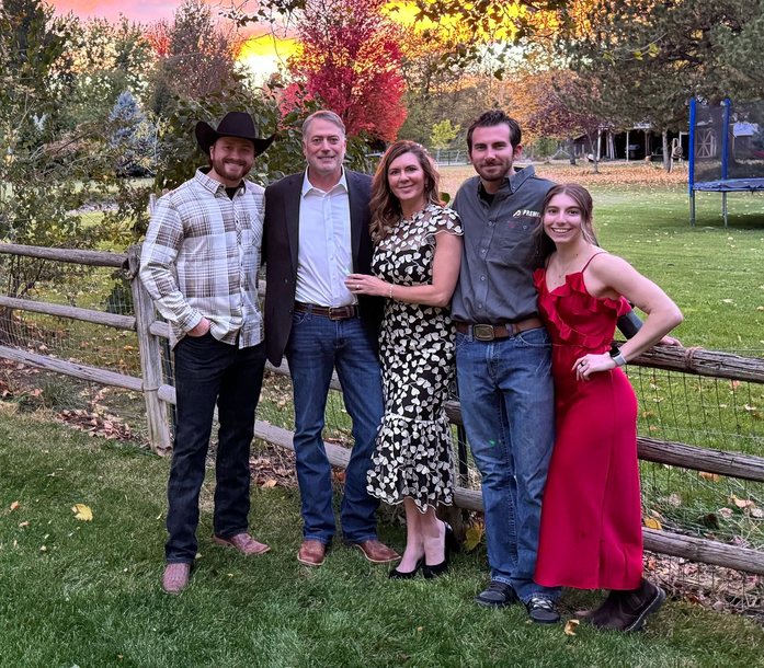 Five people posing outdoors at sunset, dressed in semi-formal clothes, standing by a fence.