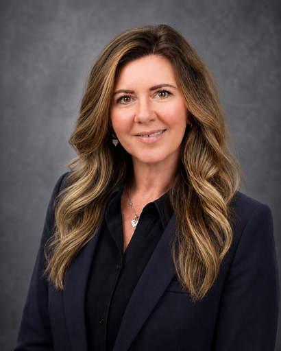 Studio headshot of a woman in a dark blazer against a gray background, smiling at the camera