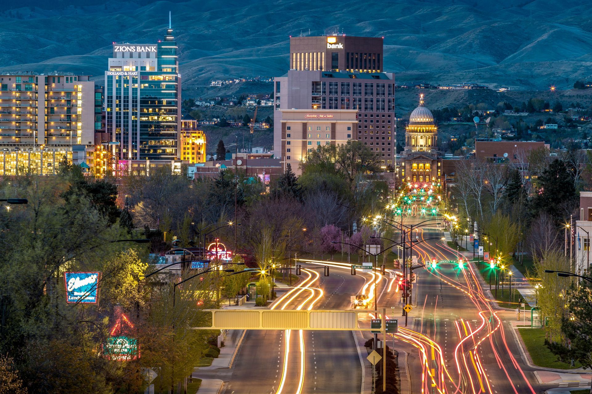 City skyline at dusk with lit buildings and traffic light trails on a curving road