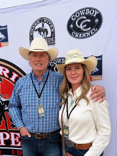 Two people posing at a Cowboy Channel event backdrop, both wearing cowboy hats and smiling.