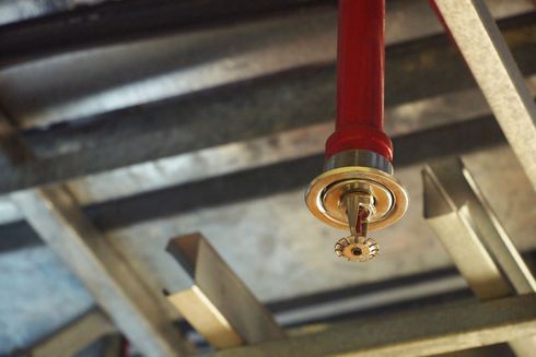 Ceiling-mounted red fire sprinkler head with a gold deflector on a metal beam ceiling