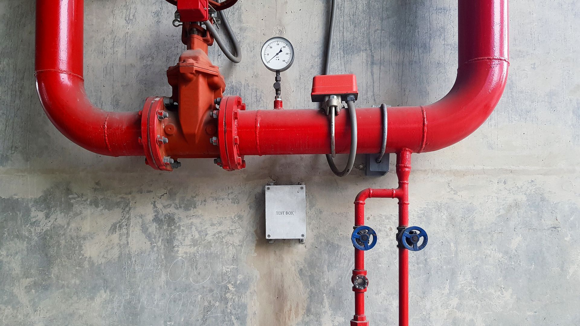 Red fire sprinkler pipes with gauges and valves mounted on a concrete wall