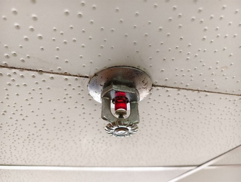 Close-up of a ceiling sprinkler head with a red glass bulb mounted on a textured white ceiling