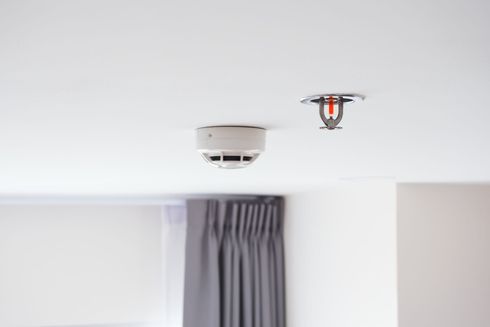 Ceiling smoke detector and sprinkler head in a white room above a curtain