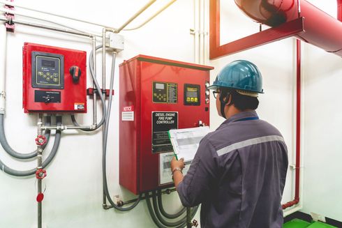 Worker in hard hat inspecting red electrical control panels in an industrial room
