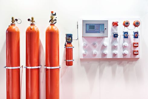 Red fire suppression cylinders beside a wall-mounted control panel with gauges and switches