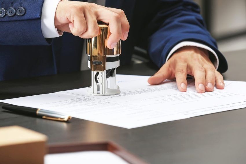 Hands stamping a document on a desk with a pen nearby