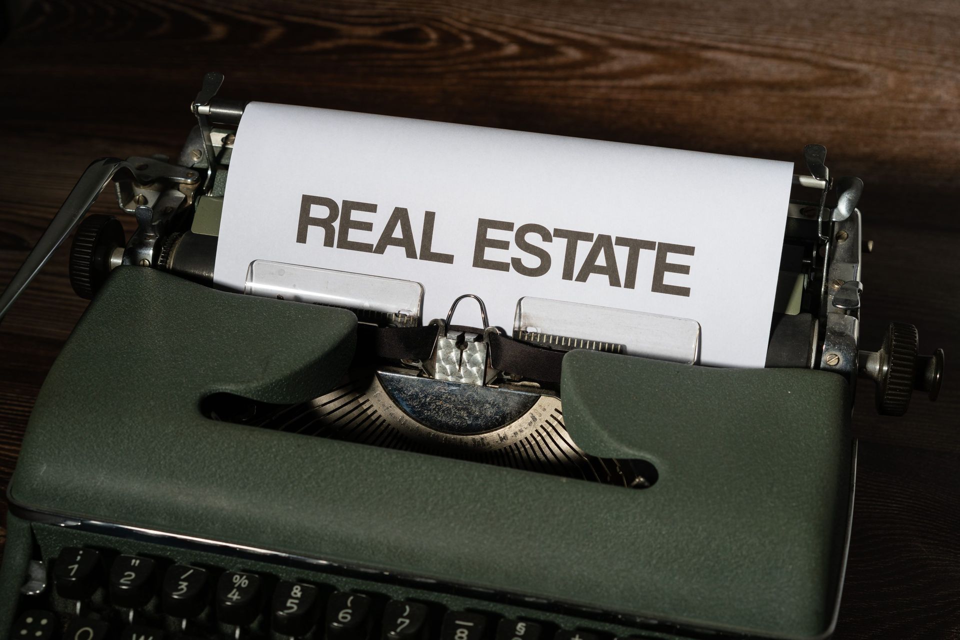 Typewriter with a paper reading “REAL ESTATE” on a dark wooden desk.