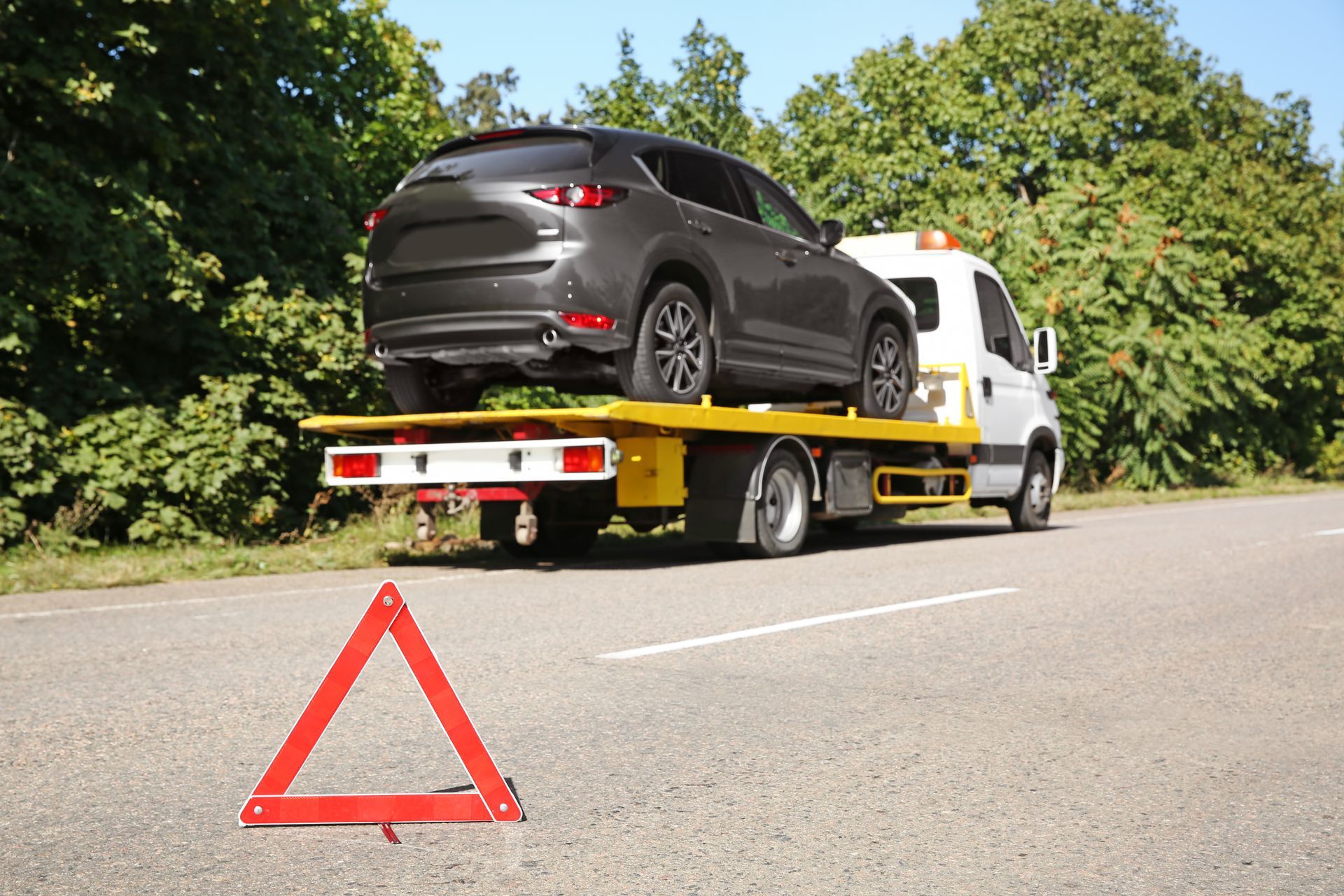 Tow truck carrying a black SUV on a roadside with a red warning triangle in front