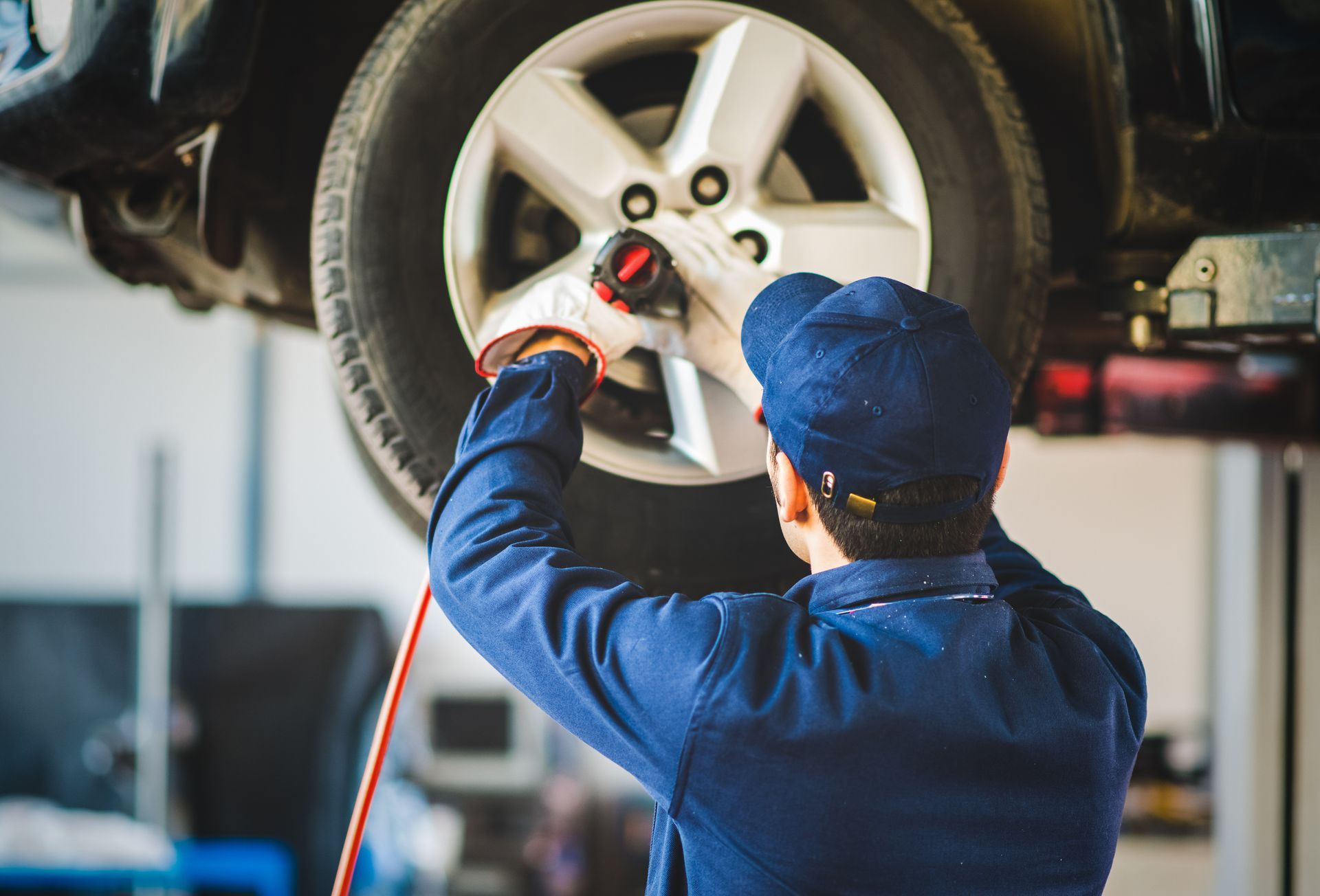 Mechanic using a red air hose to service a car tire on a lift