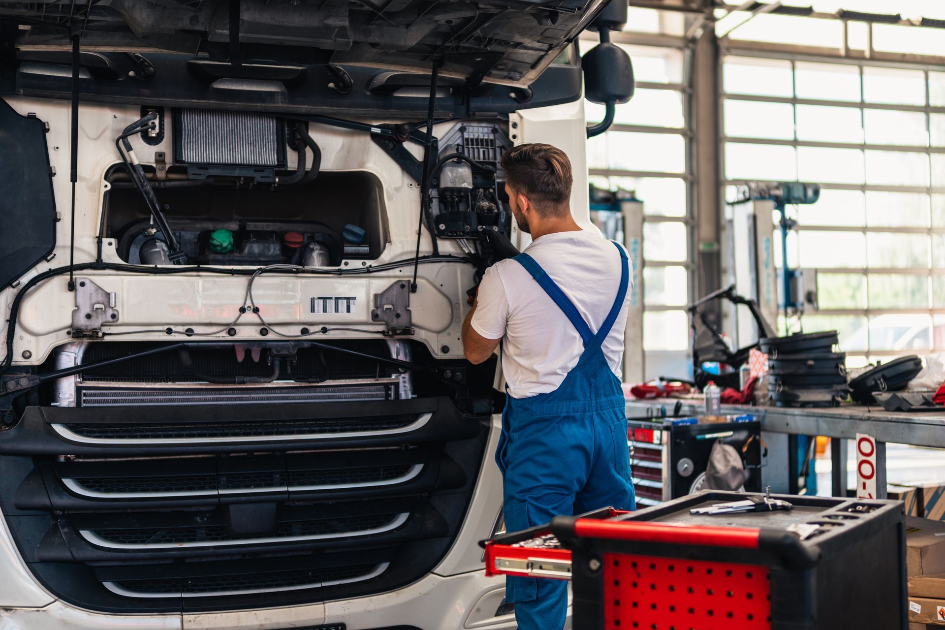 Mechanic inspecting a white truck engine in a repair garage, with tools and equipment nearby
