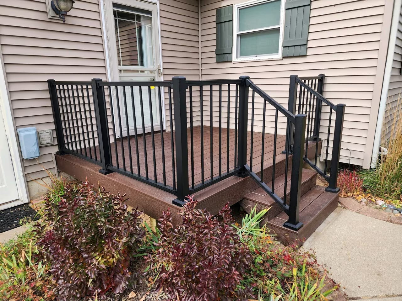 Raised wooden deck with black railings and a ramp beside a house entrance