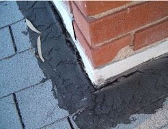 Close-up of a brick wall corner with white sealant along the base beside dark paving stones.