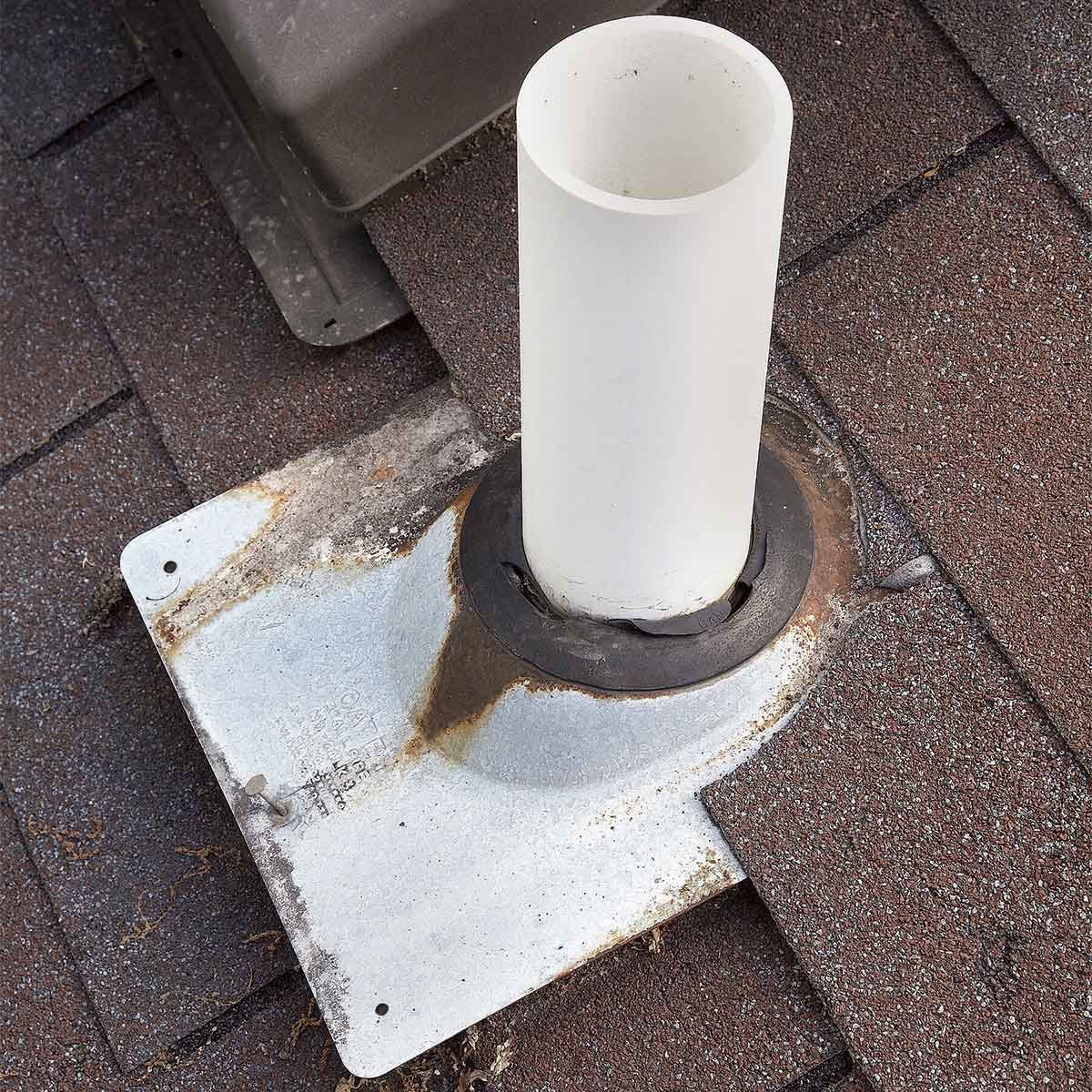 Roof vent pipe with a white flashing base on brown shingles, showing rust and weathering