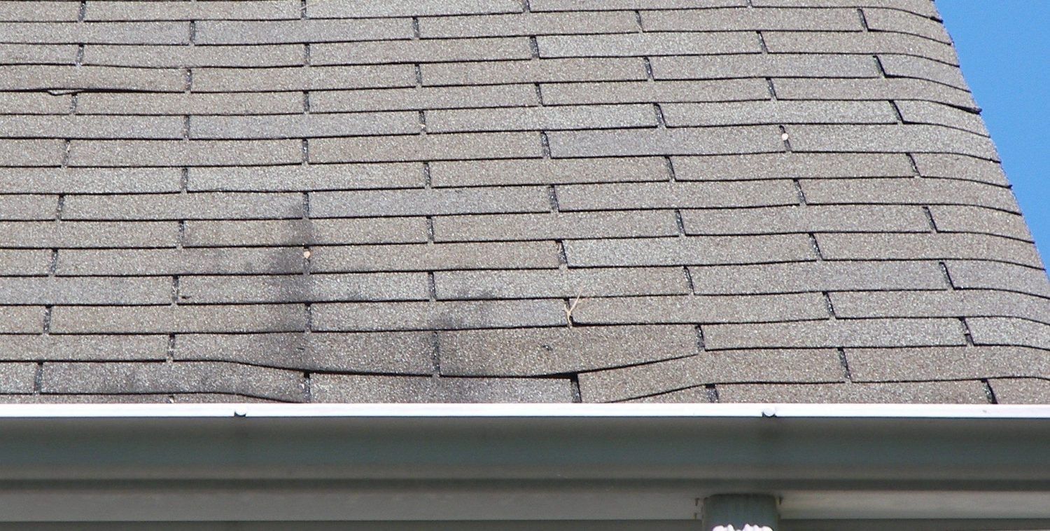 Close-up of a gray shingled roof with white gutter and blue sky visible at the edge