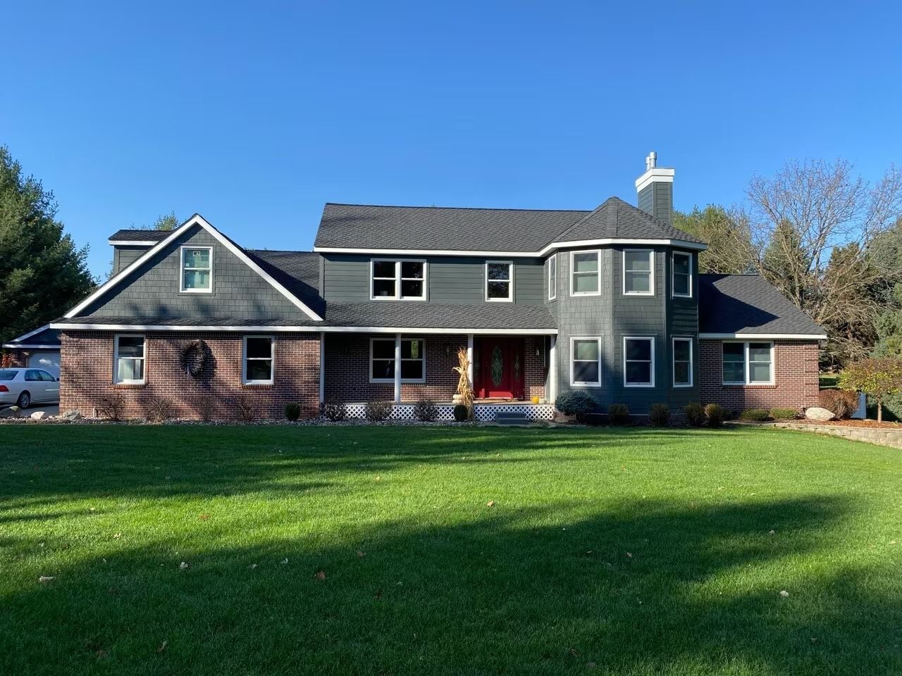 Suburban house with gray siding, brick accents, and a large green lawn under a clear blue sky