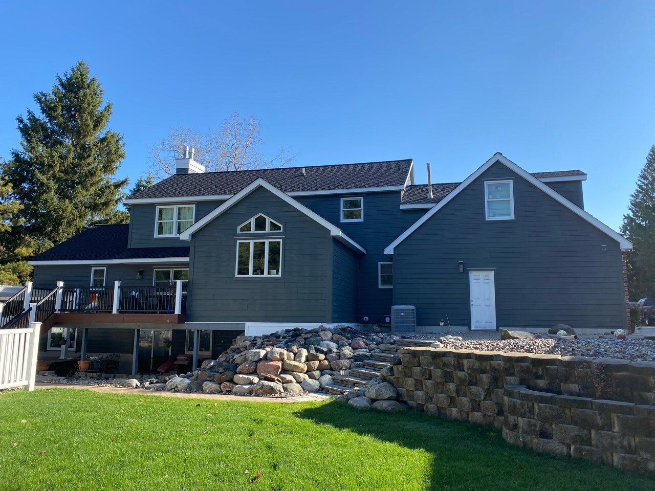 Blue-gray house with white trim and stone retaining wall under a bright blue sky
