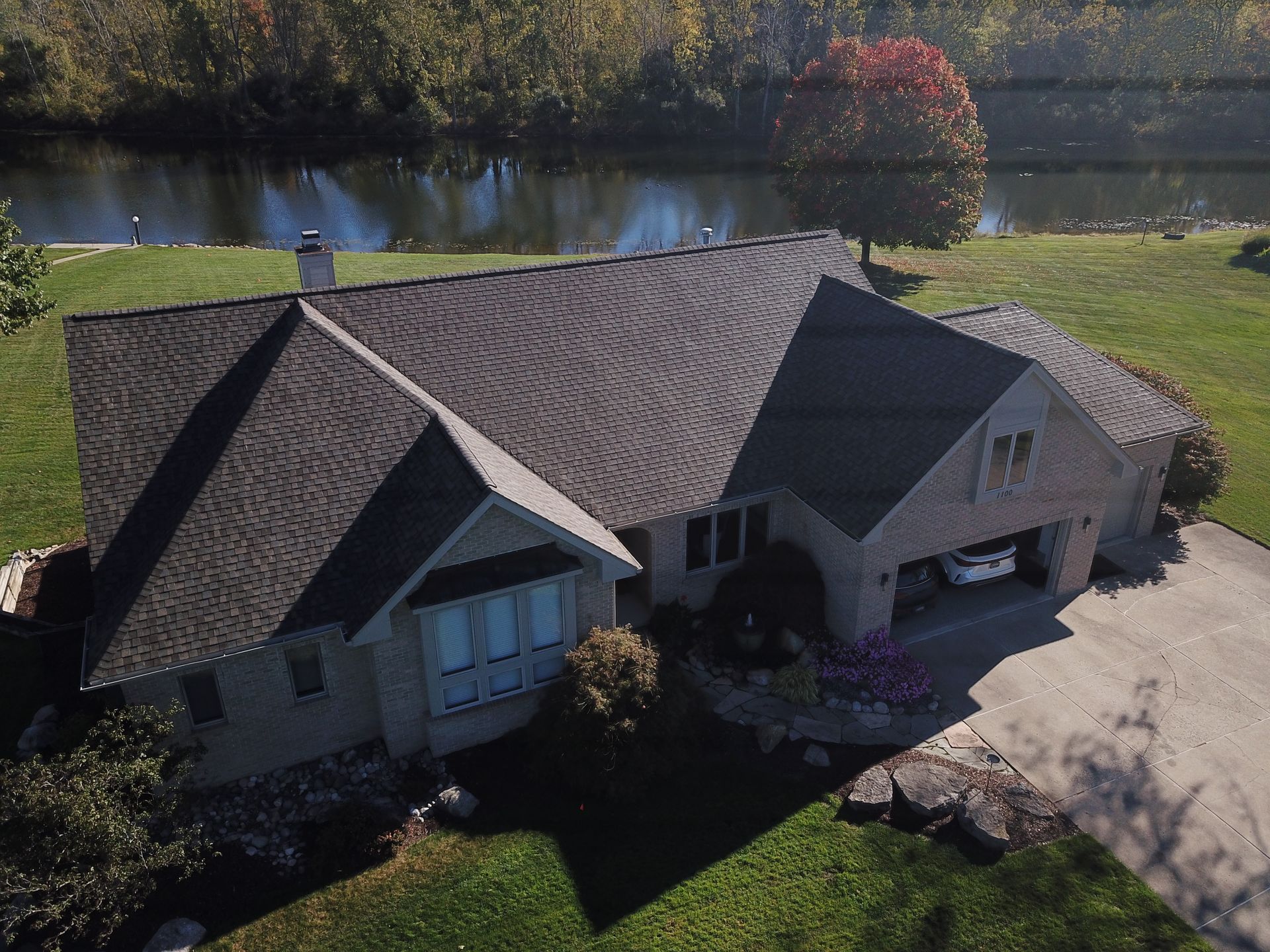 Aerial view of a house with a dark roof beside a driveway and pond