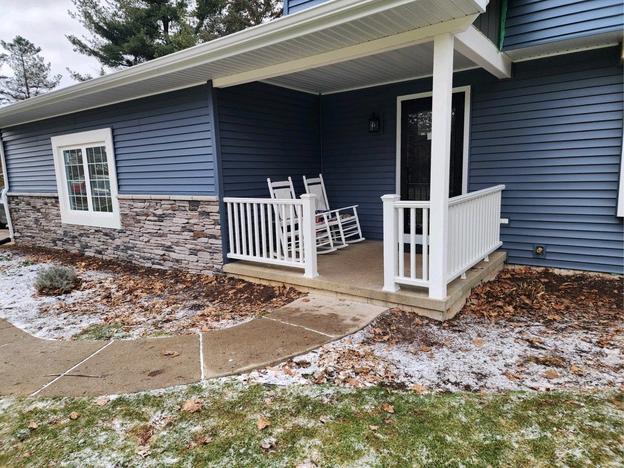 Blue house exterior with a small front porch, white railing, chairs, and light snow on the ground
