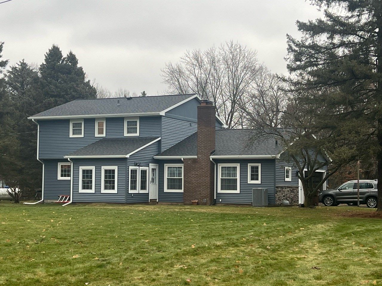 Blue two-story house with white trim, large lawn, and leafless trees on an overcast day