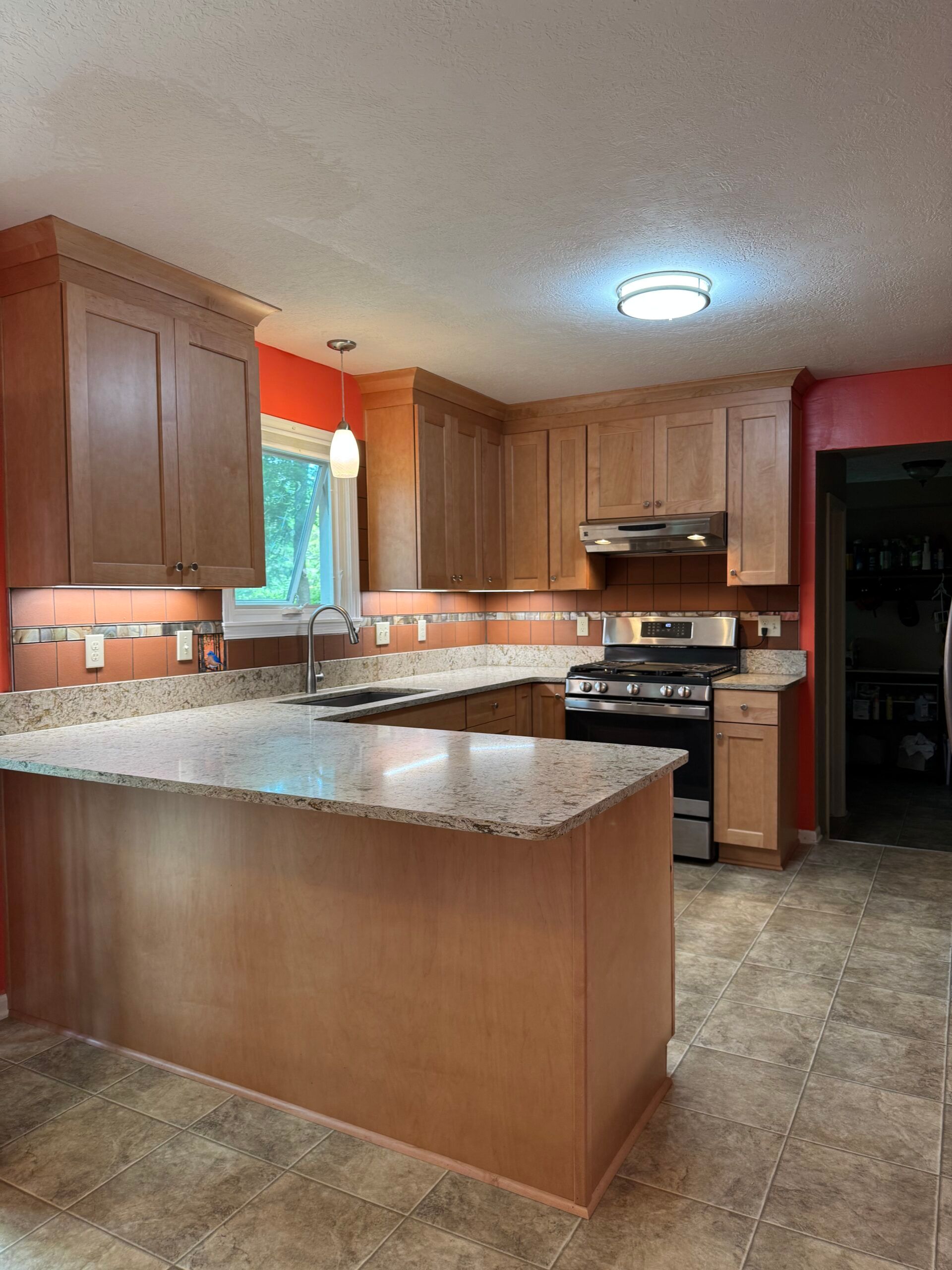 Kitchen with light wood cabinets, granite countertops, and orange walls.