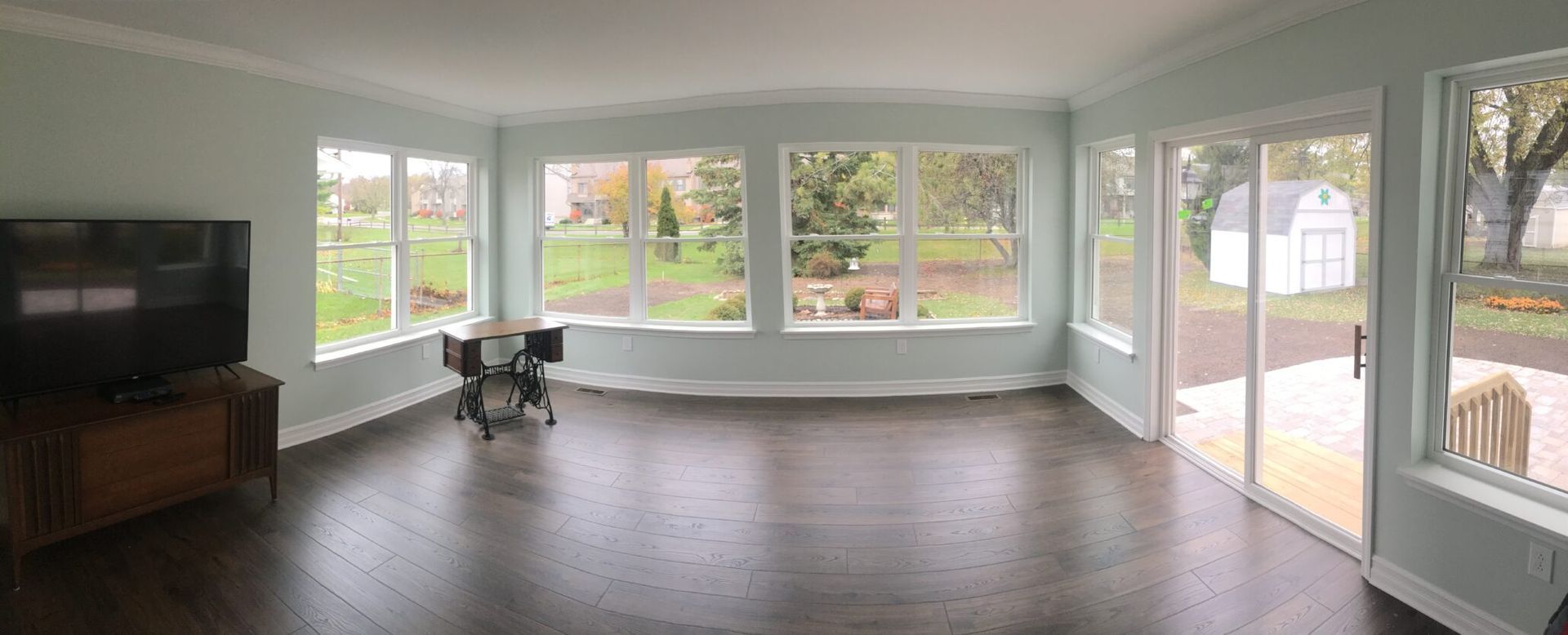 Sunroom with large windows, sliding door, dark wood floor, and a TV on a wooden stand.