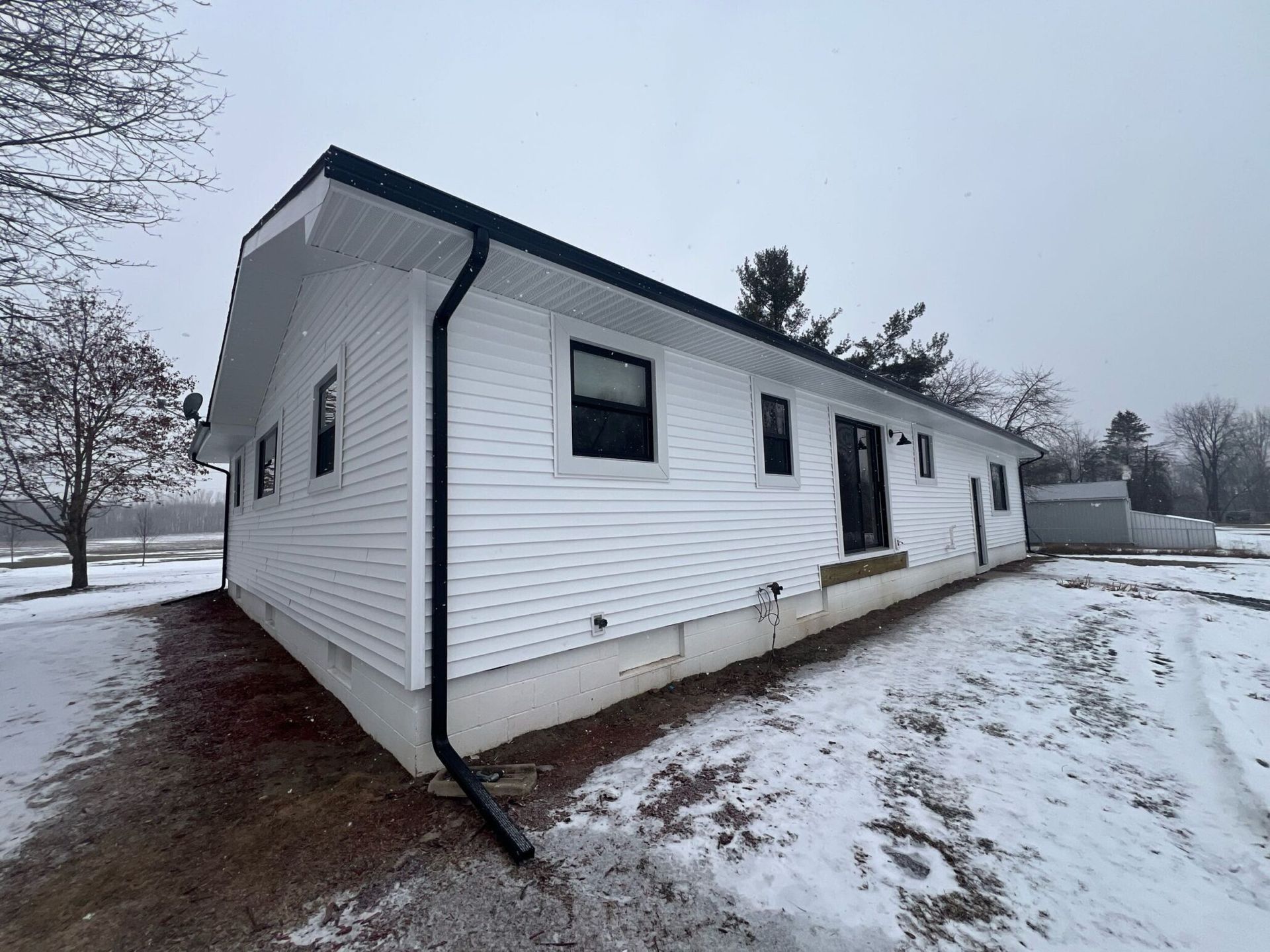 White house with black trim and gutters, sitting in a snowy landscape.