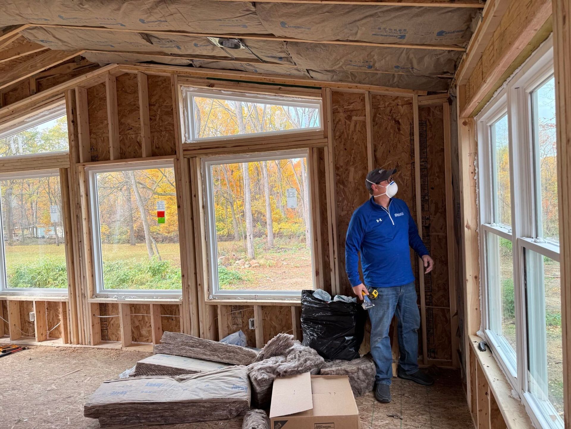 Man in face mask inspects a room under construction with windows and insulation.