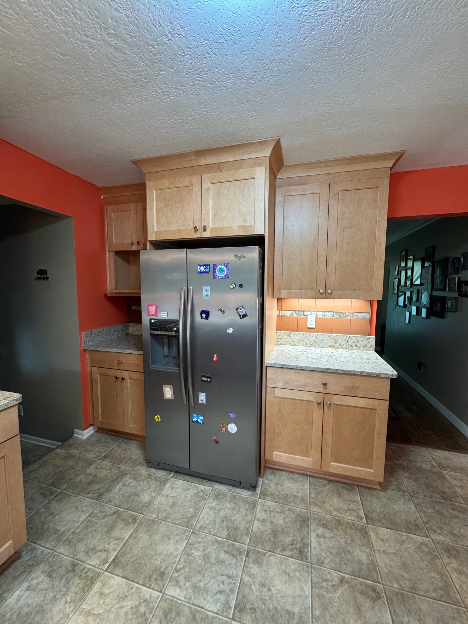 Kitchen with light wood cabinets, stainless steel refrigerator, and orange wall.