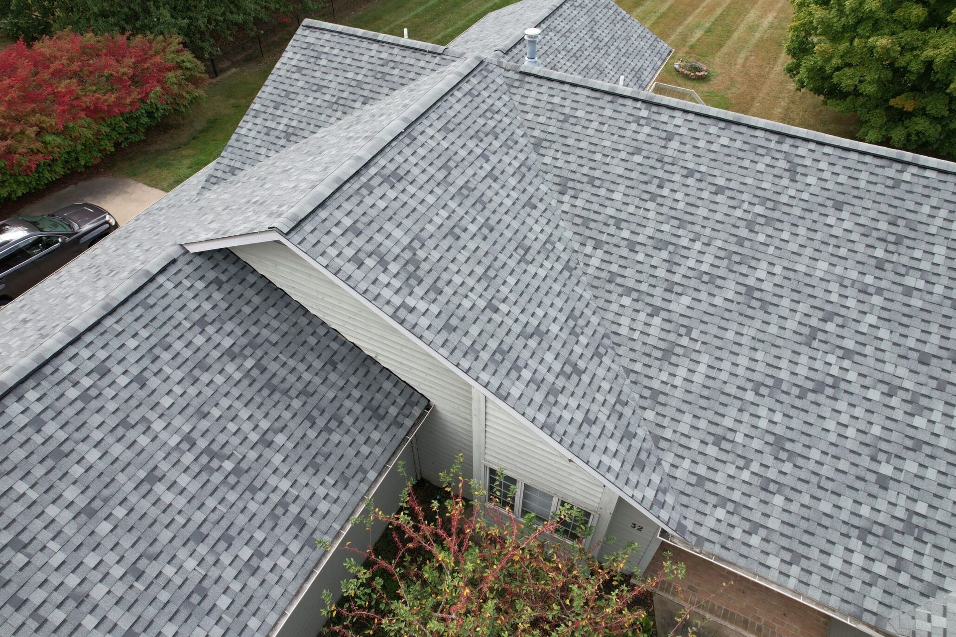 Aerial view of a gray shingled house roof with a dormer and surrounding greenery