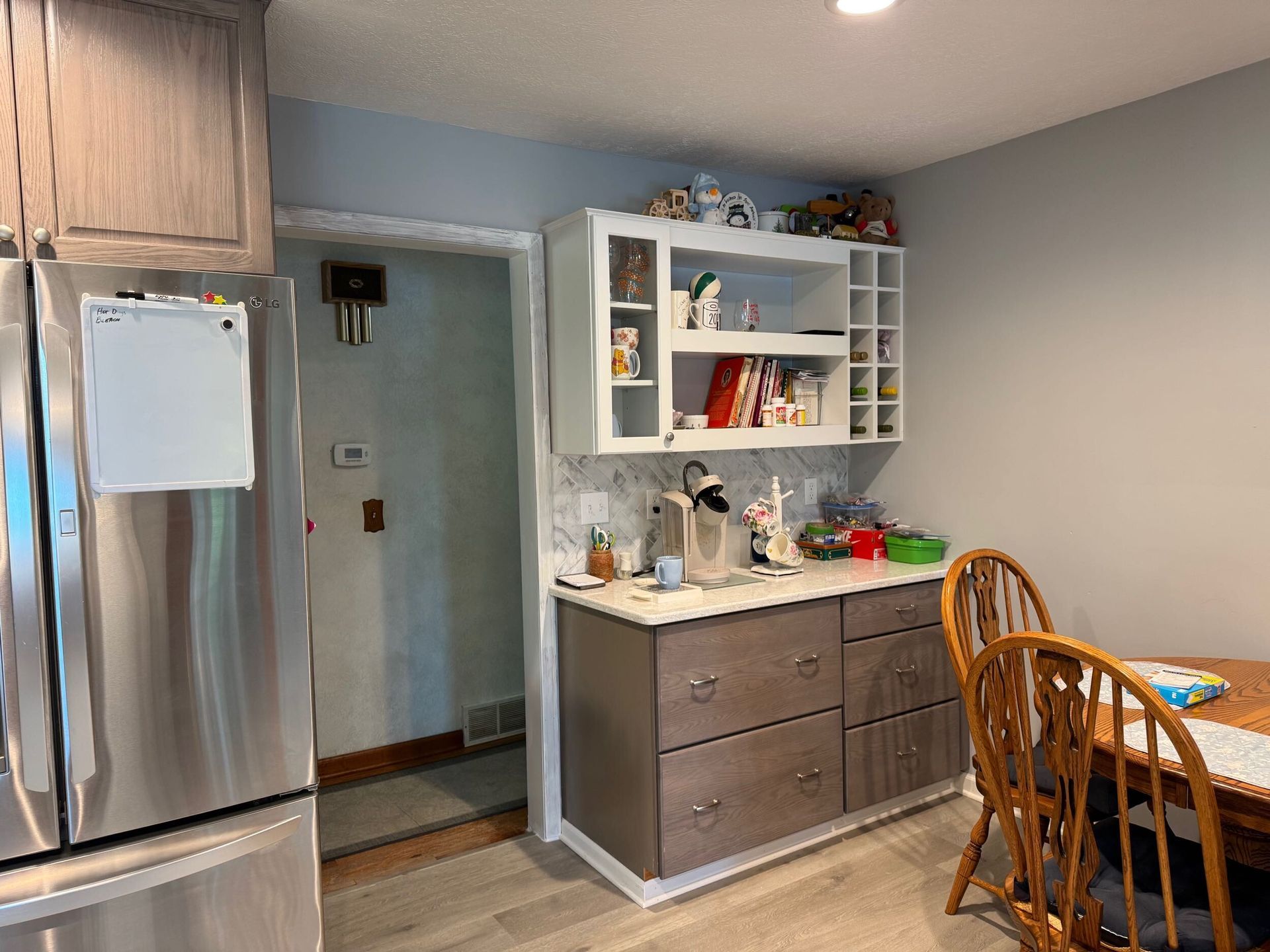 Kitchen with gray cabinetry, a refrigerator, a built-in cabinet with open shelving, and a wooden table.