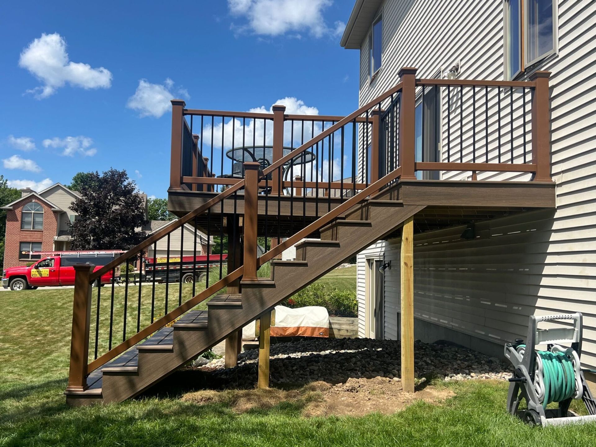 Backyard wooden deck staircase with railing beside a house, over grassy yard under a blue sky.