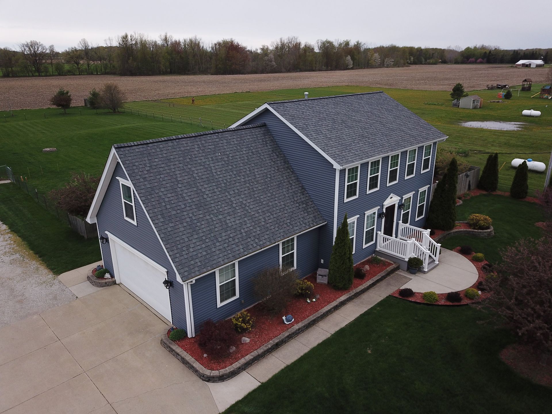 Aerial view of a blue two-story house with a gray roof, white trim, and landscaped front yard.