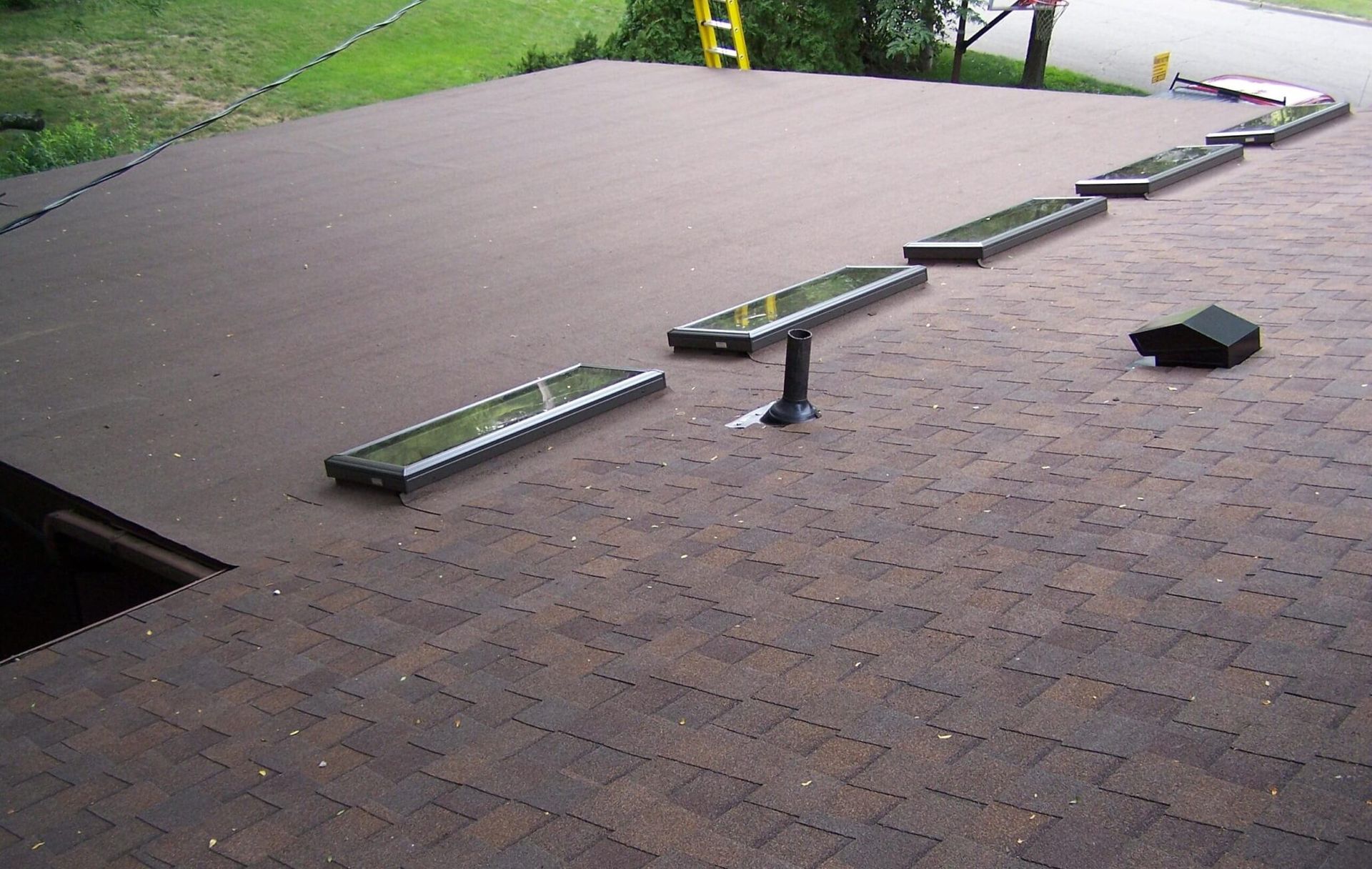 Rooftop with a long narrow bench and skylights on a brown shingle surface.