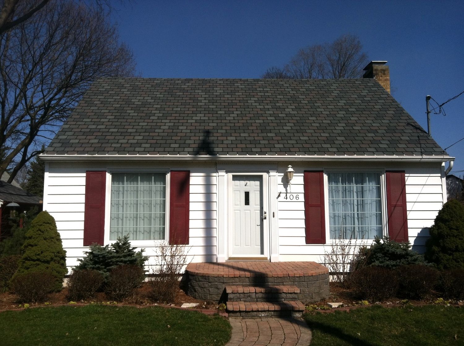 Small white house with red shutters, a central front door, and a stone walkway under a blue sky