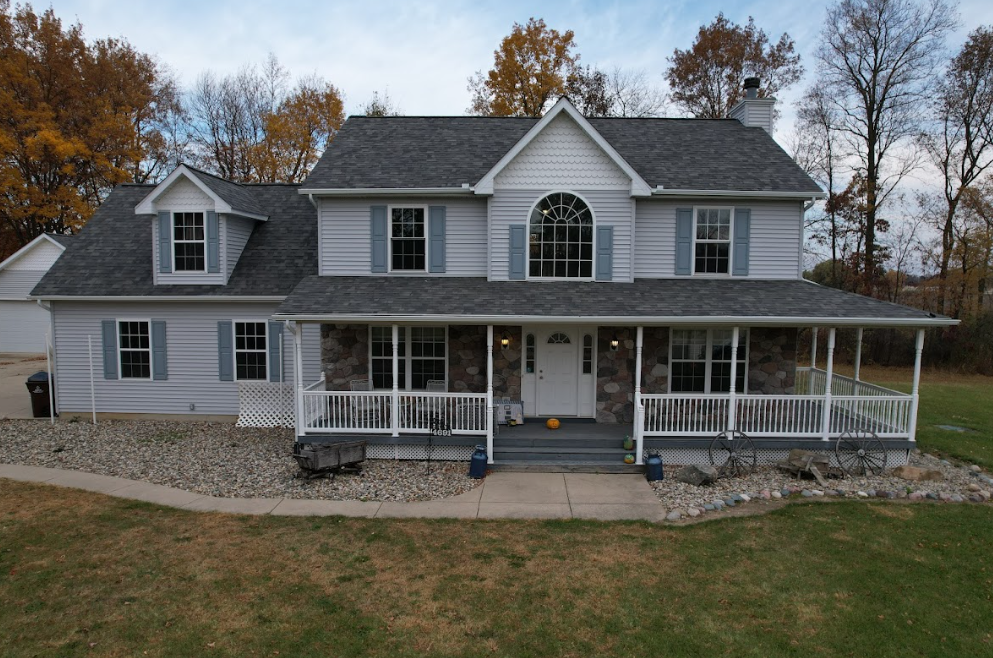 Gray two-story house with a large front porch and autumn trees in the yard