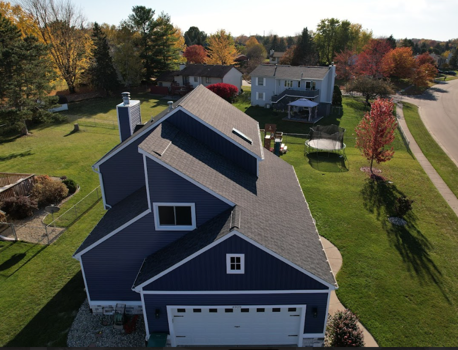 Aerial view of a gray suburban house with a garage, surrounded by autumn trees and a lawn.