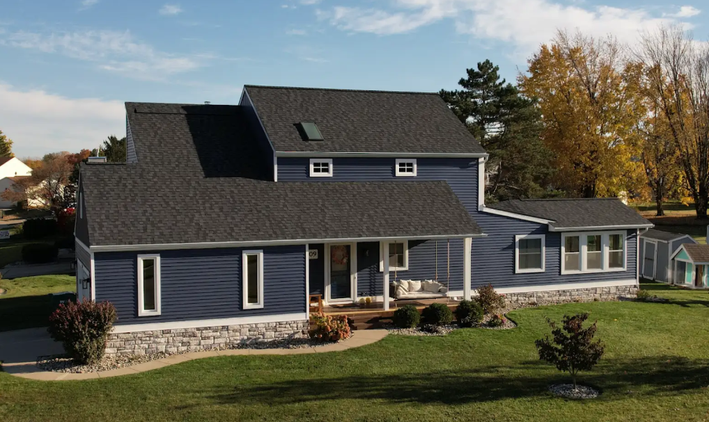 Blue two-story house with black roof, white trim, and a front porch on a grassy lawn