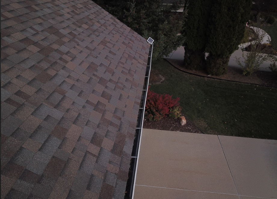 Roof edge with shingles overlooking a driveway, lawn, and bushes below