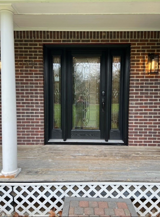 Black front door with sidelights, brick exterior, white porch columns, and decorative lattice.