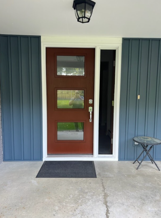 Red door with three glass panels, white trim, blue siding, concrete porch, black doormat.