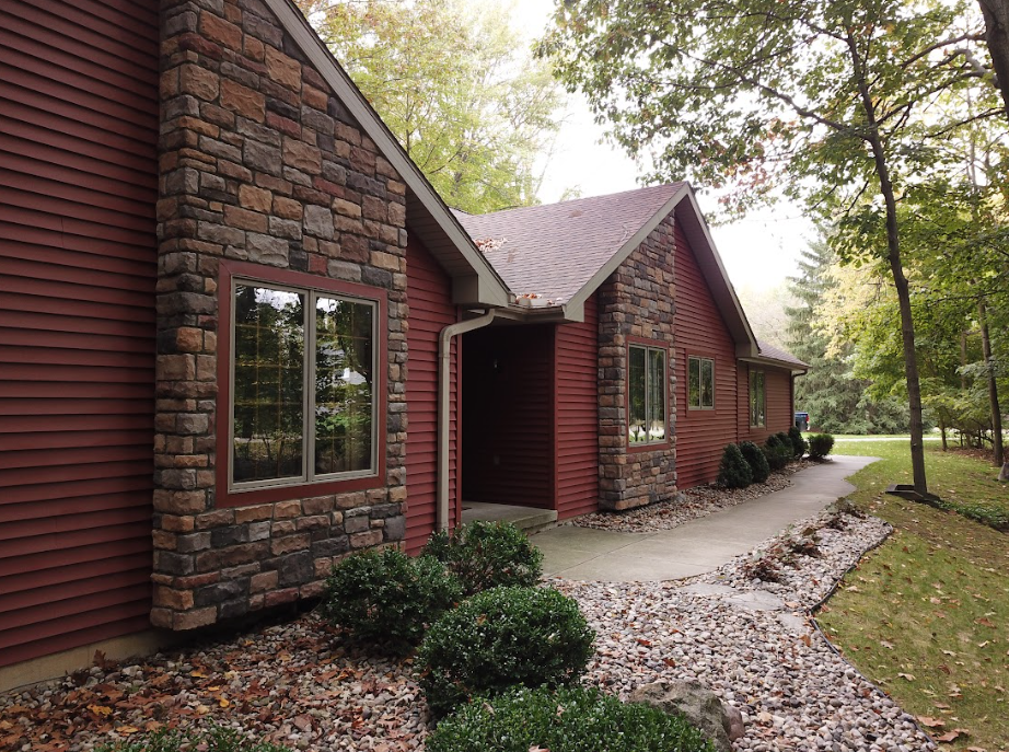 Brick house exterior with large windows, stone accents, and a curved gravel path under trees