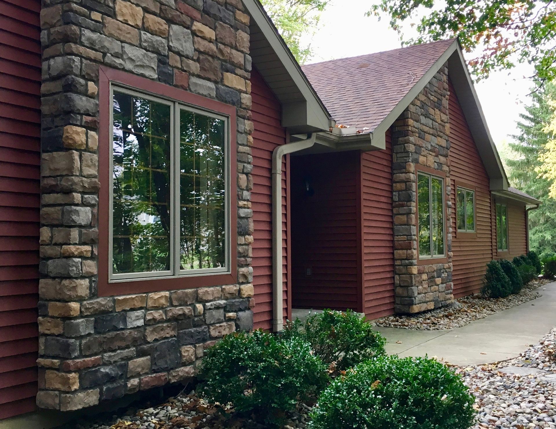 Brick house exterior with stone accents, red siding, windows, and a front walkway