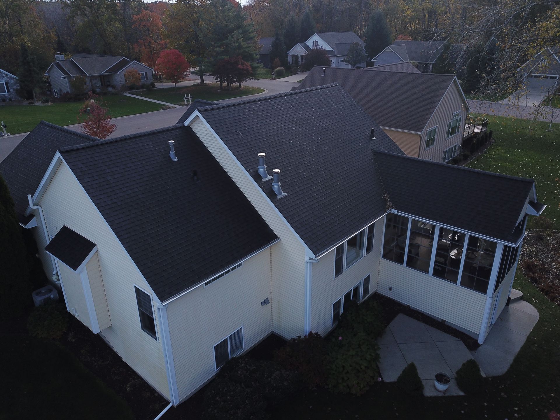 Aerial view of a white house with a dark roof in a suburban neighborhood