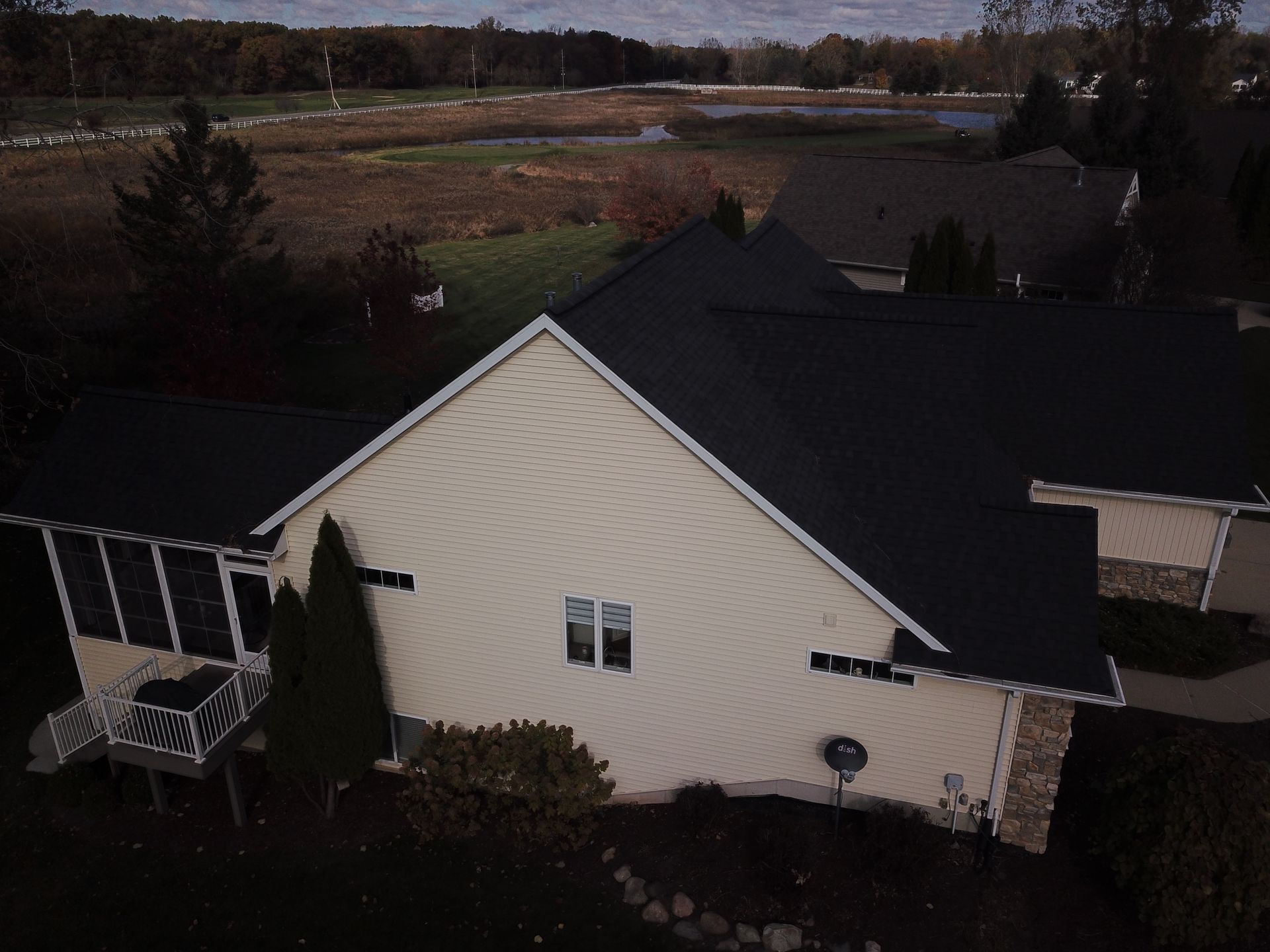 Aerial view of a cream house with a dark roof, surrounded by trees and open fields at dusk
