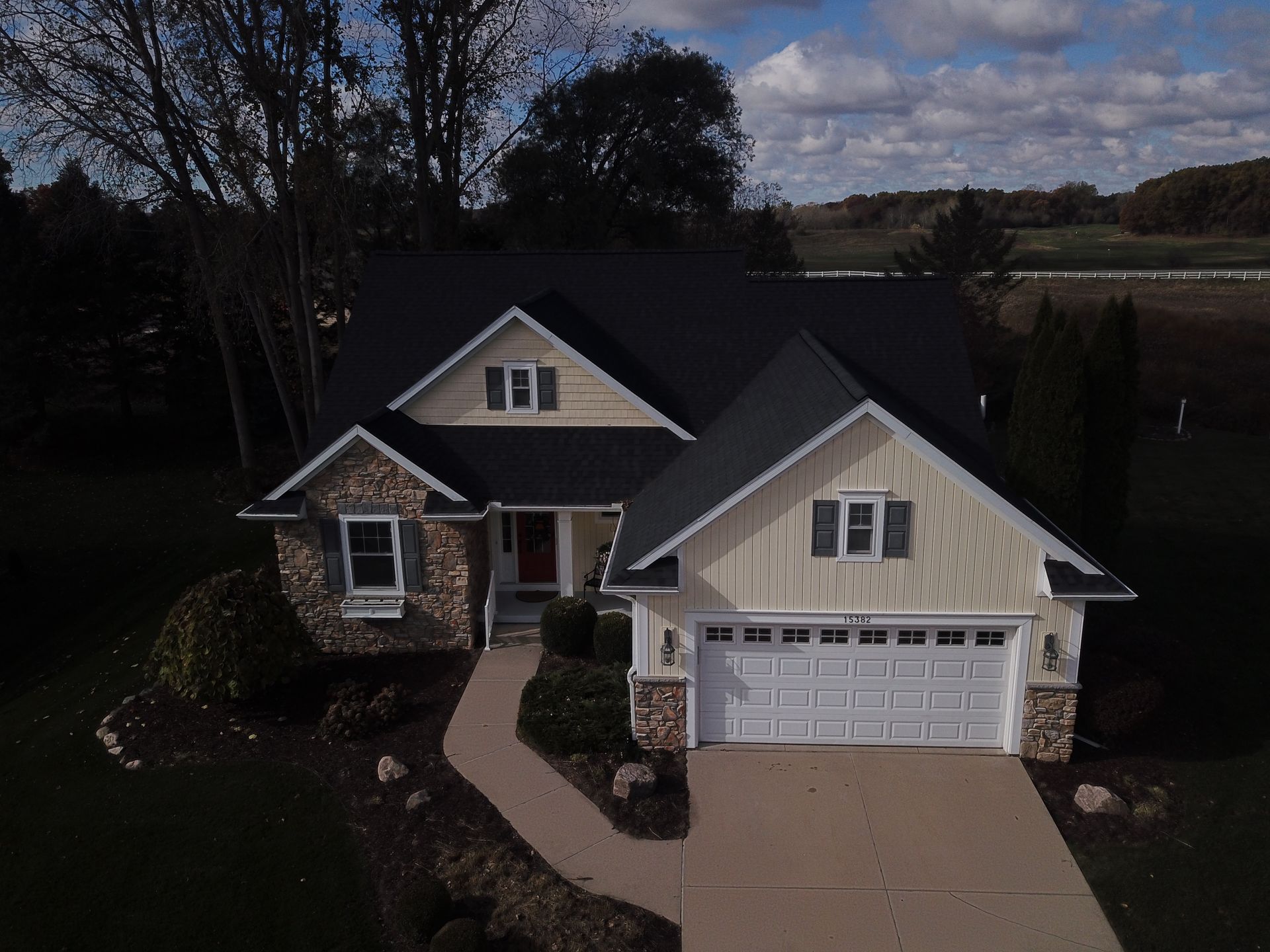 A beige suburban house with a dark roof, front porch, garage, and curved walkway at dusk.