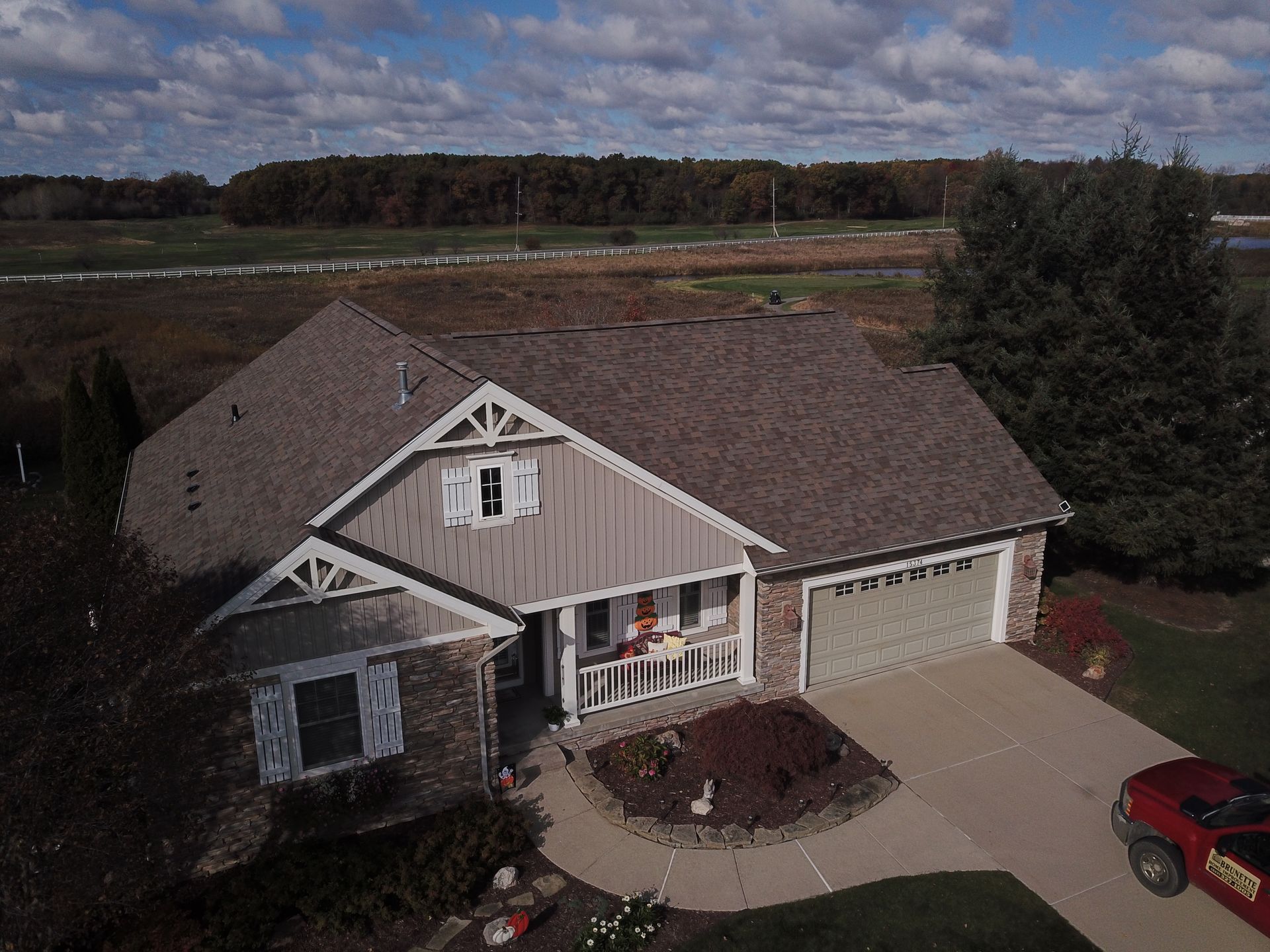 Suburban house with stone-and-siding exterior, two-car garage, driveway, and a red car parked beside it